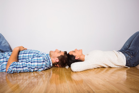 Young couple lying on floor smiling at homeの写真素材