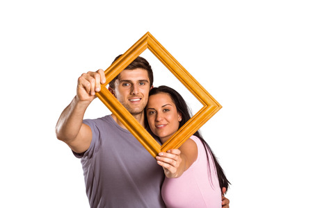 Young couple holding up frame on white backgroundの写真素材