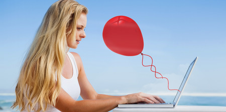 Composite image of pretty blonde using her laptop at the beach against red balloonの写真素材
