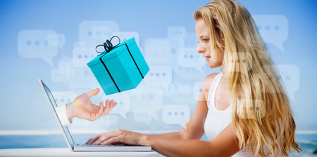 Composite image of pretty blonde using her laptop at the beach with hand presenting giftの写真素材