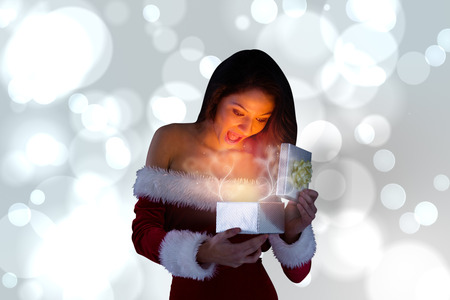 Sexy santa girl opening gift against white glowing dots on greyの写真素材