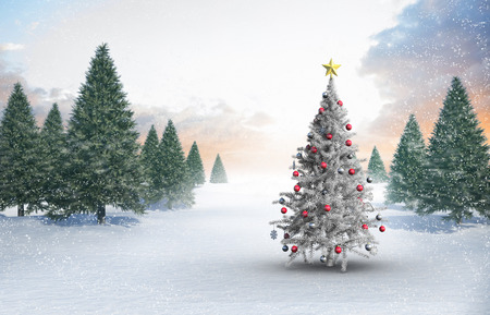 Christmas tree with baubles and star against snowy landscape with fir treesの写真素材