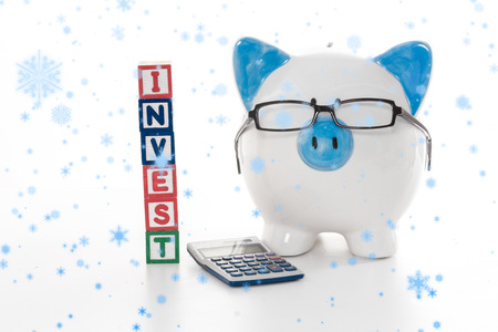 Snow falling against blue and white piggy bank wearing glasses with invest building blocksの写真素材