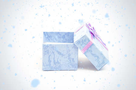 Snow falling against blue gift box with purple ribbon leaning against anotherの写真素材