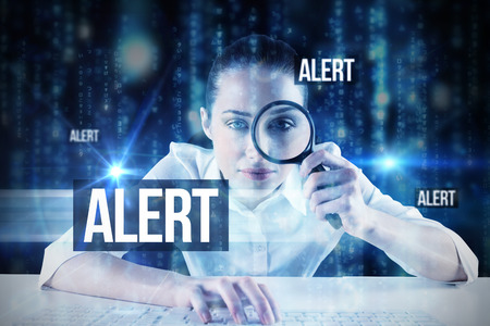 The word alert and businesswoman typing and looking through magnifying glass against lines of blue blurred letters fallingの写真素材