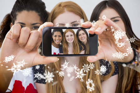 Hand holding smartphone showing close up portrait of cheerful female friendsの写真素材