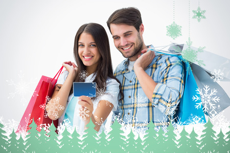 Attractive young couple with shopping bags and credit card against snowflakes and fir trees in greenの写真素材
