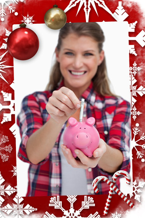 Portrait of a woman putting a note a piggy bank against christmas themed pageの写真素材