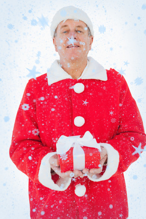 Festive man holding christmas gift against snow fallingの写真素材