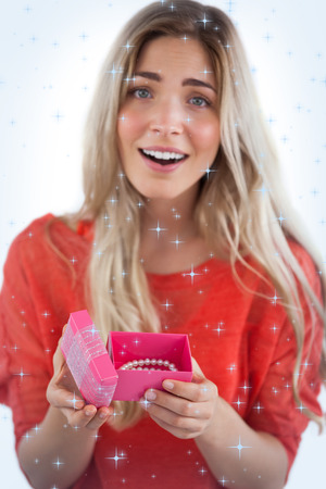 Composite image of Surprised blonde woman opening gift with twinkling starsの写真素材