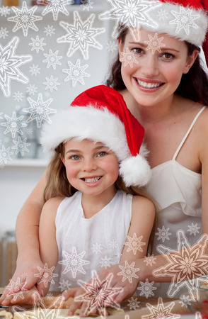 Smiling mother and daughter baking Christmas cakes against snowflakes on silverの写真素材