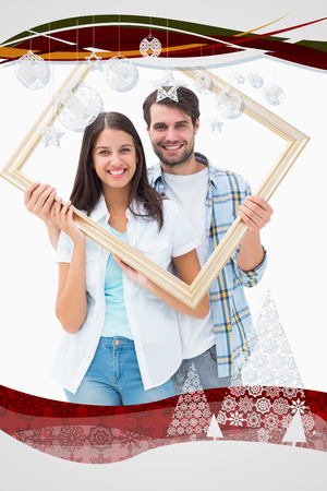 Happy young couple holding picture frame against christmas frameの写真素材
