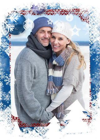 Smiling couple standing on the beach in warm clothing against christmas themed frameの写真素材