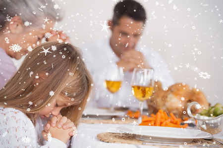 Composite image of Little girl saying grace with family  against snow fallingの写真素材