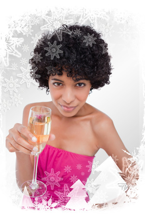 Young woman holding a glass of champagne while looking at the camera against christmas frameの写真素材