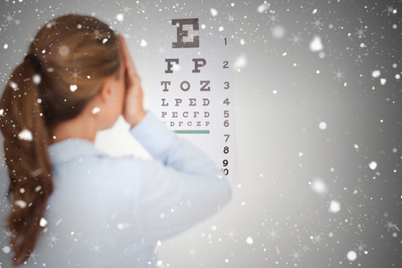 Composite image of brunette woman making an eye test against snow falling