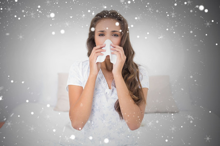 Composite image of pretty brunette blowing her nose against snowの写真素材