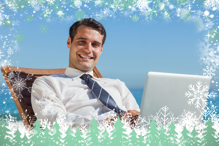Cheerful young businessman lying on a deck chair with his computer against snowの写真素材