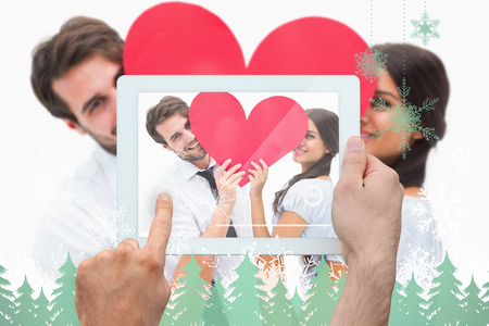 Hand holding tablet pc against snowflakes and fir trees in greenの写真素材