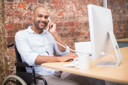 Businessman in wheelchair working at his desk on the phone in the office