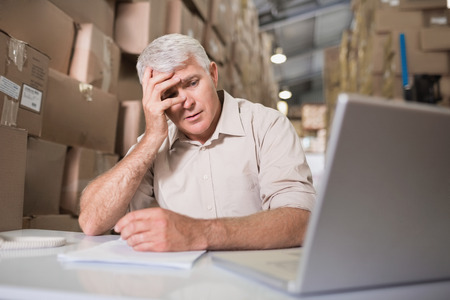 Worried warehouse manager with laptop sitting at desk