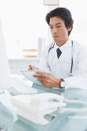 Focused doctor writing down notes while sitting downの写真素材