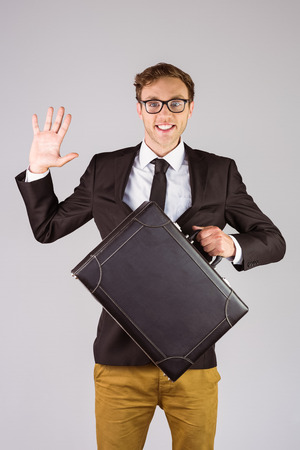 Young geeky businessman holding briefcase on grey backgroundの写真素材