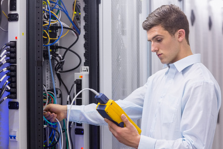Focused technician using digital cable analyser on servers in a large data center