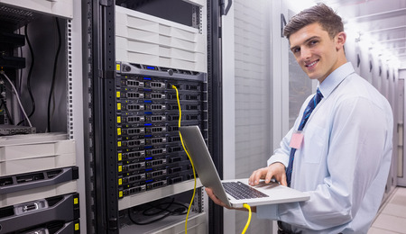 Smiling technician using laptop while analysing server in large data center