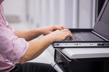 Close up of technician sitting using laptop to diagnose servers in large data center