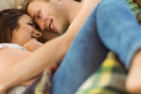 Cute couple cuddling on couch at home in the living roomの写真素材