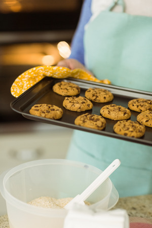 Woman showing tray of fresh cookies at home in the kitchenの写真素材