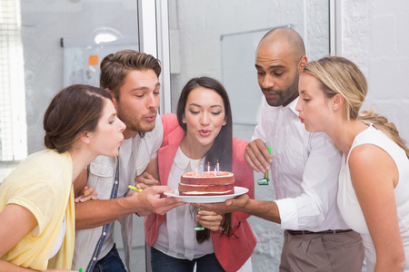 Businesswoman blowing the candles on her birthday cake in the officeの写真素材