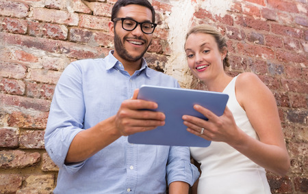 Two business people using digital tablet against brick wall in officeの写真素材