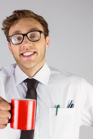 Young geeky businessman holding mug on grey backgroundの写真素材