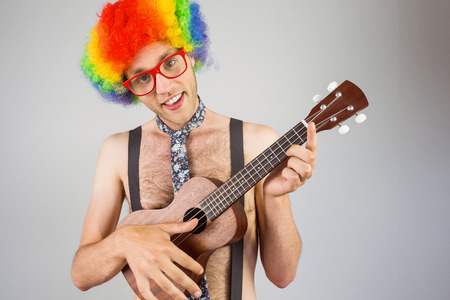 Geeky hipster in afro rainbow wig playing guitar on grey background