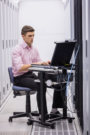 Technician sitting on swivel chair using laptop to diagnose servers in large data centerの写真素材