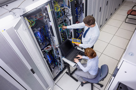 Team of technicians using digital cable analyser on servers in large data center