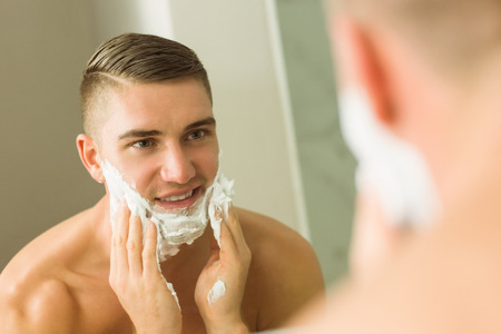Man putting shaving foam on face at home in the bathroomの写真素材