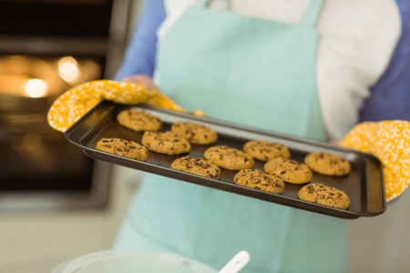 Woman showing tray of fresh cookies at home in the kitchenの写真素材