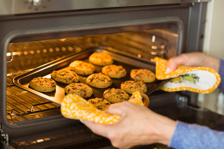 Woman taking tray of fresh cookies out of oven at home in the kitchenの写真素材