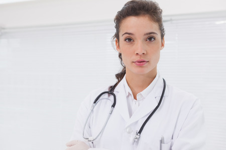 Concentrated doctor standing with stethoscope in medical officeの写真素材