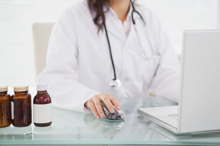 Doctor using laptop near pill bottles in medical officeの写真素材