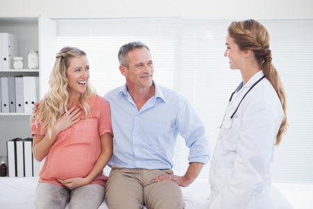 Happy couple talking to doctor about pregnancyの写真素材