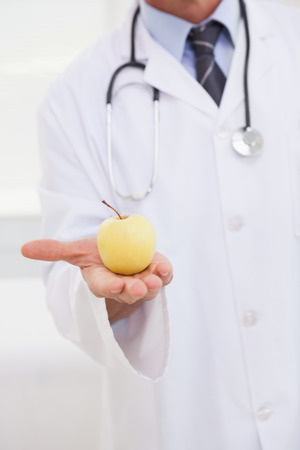 Doctor holding an apple in his hand towards the cameraの写真素材