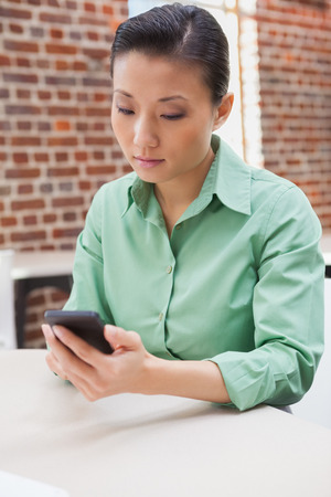 Casual businesswoman sending a text in the officeの写真素材
