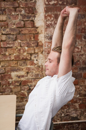 Man sitting with arms raised at desk in the officeの写真素材