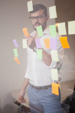 Casual businessman looking at sticky notes in the officeの写真素材