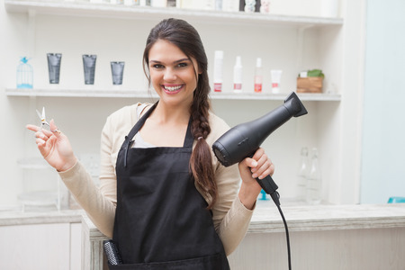 Cheerful hairdresser looking at camera holding hair equipmentの写真素材