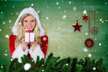 Pretty girl in santa outfit holding gift against fir tree branches and christmas decorationsの写真素材